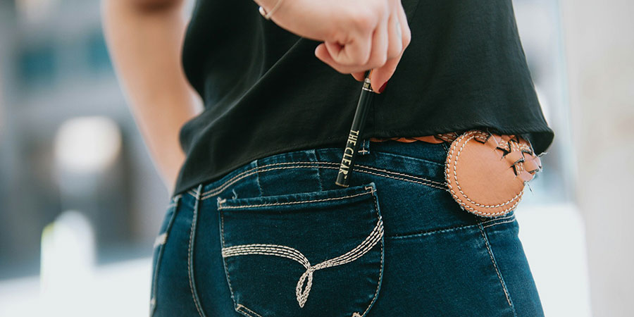 close up view of a person's hand holding The Clear Cannabis vape pen and placing it inside their denim jeans back pocket